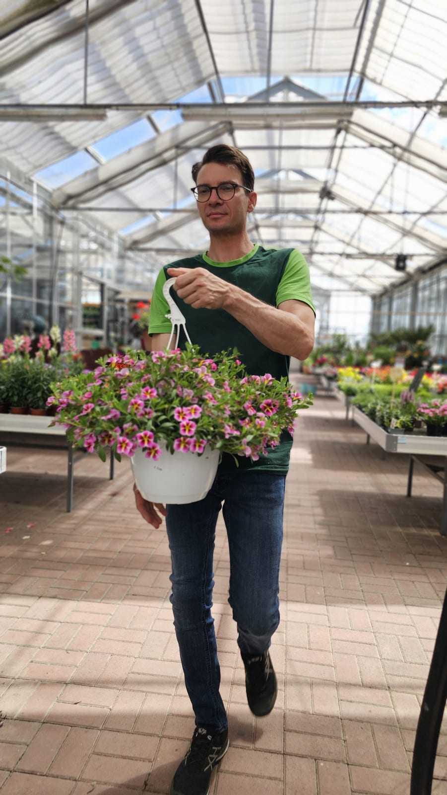Mitarbeiter präsentiert lächelnd eine blühende Blumenampel